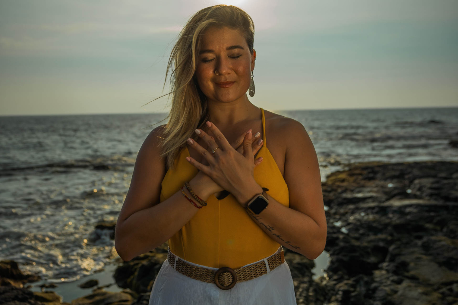 Woman standing in front of ocean with hands over heart.